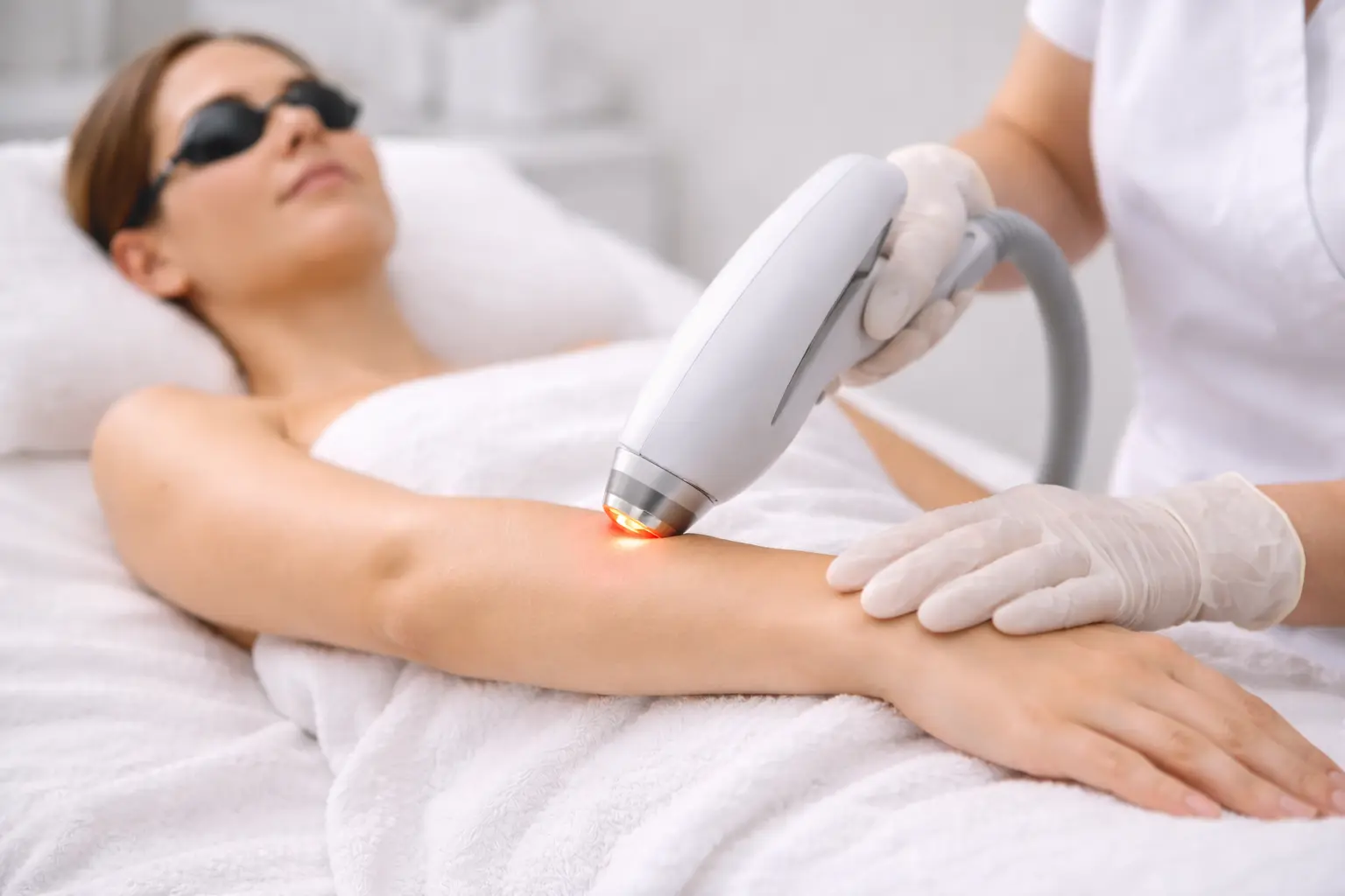 Laser treatment device applied to forearm area during professional skin treatment session with protective eyewear.